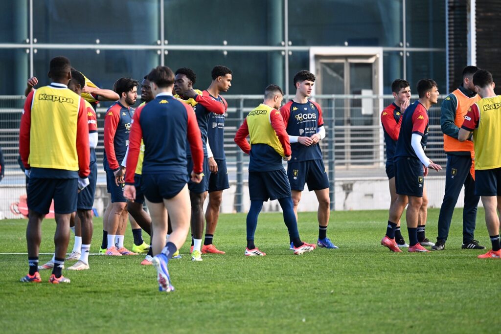 I giocatori del Genoa si confrontano sul campo durante una sessione di allenamento, con casacche rossoblù e gialle.