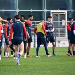 I giocatori del Genoa si confrontano sul campo durante una sessione di allenamento, con casacche rossoblù e gialle.