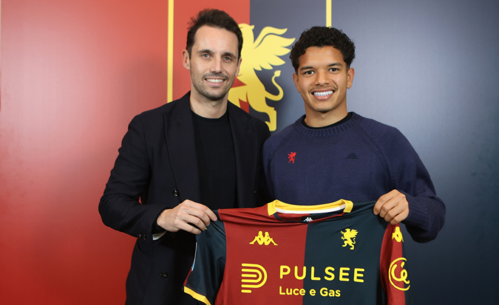 Due uomini sorridenti posano davanti al logo del Genoa e tengono una maglia rossoblù con sponsor Pulsee Luce e Gas, mentre Alexsandro Amorim è al centro.