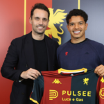 Due uomini sorridenti posano davanti al logo del Genoa e tengono una maglia rossoblù con sponsor Pulsee Luce e Gas, mentre Alexsandro Amorim è al centro.