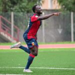 Seydou Fini corre sorridendo e punta il dito in campo con la maglia rossoblù del Genoa durante un allenamento.