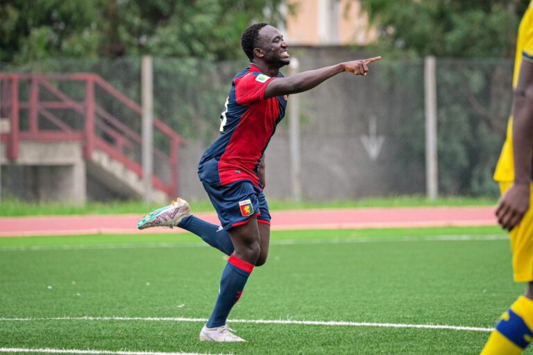 Seydou Fini corre sorridendo e punta il dito in campo con la maglia rossoblù del Genoa durante un allenamento.
