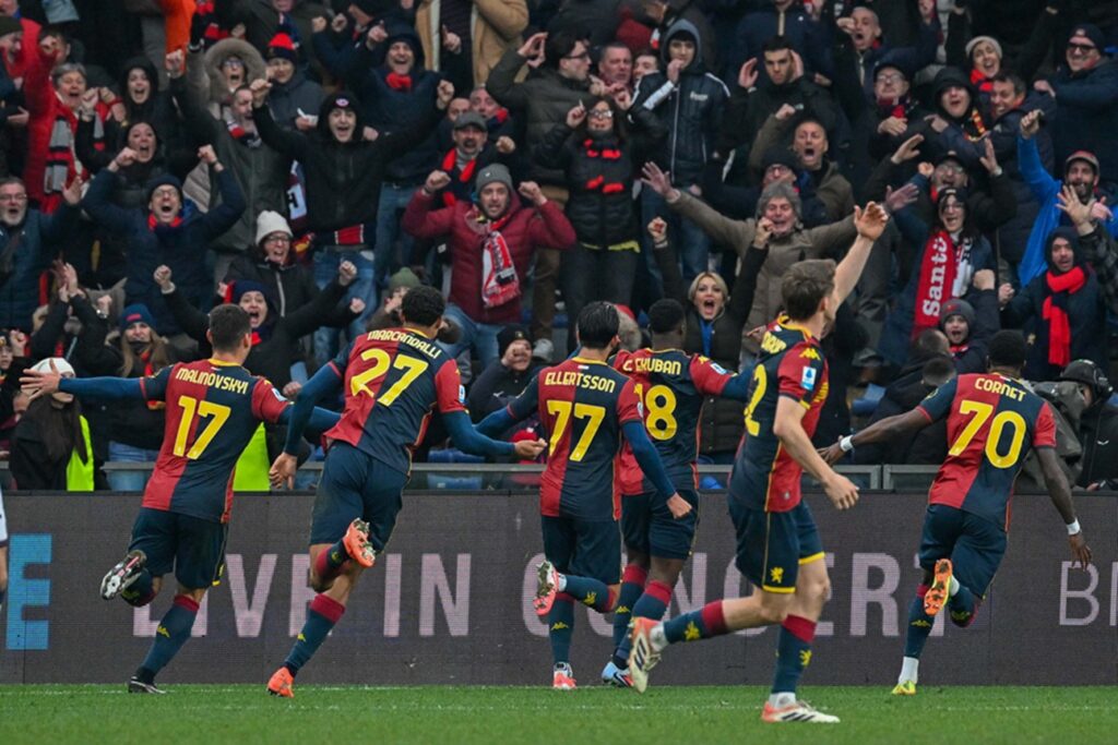 I giocatori del Genoa corrono sotto la curva dopo un gol, con i tifosi in festa alle loro spalle.