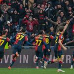I giocatori del Genoa corrono sotto la curva dopo un gol, con i tifosi in festa alle loro spalle.