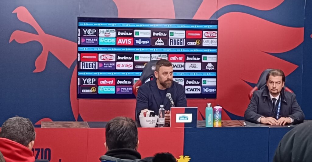 De Rossi parla in conferenza stampa dopo Genoa-Bologna, con il richiamo a “Vivo per queste emozioni” sullo sfondo.