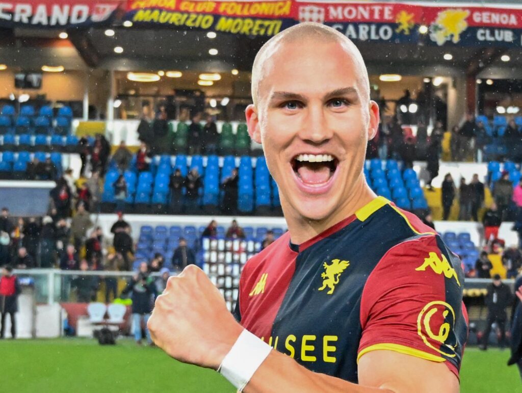 Leo Skiri Østigård sorride e alza il pugno con la maglia del Genoa CFC, davanti ai tifosi sugli spalti dello stadio durante la festa rossoblù.