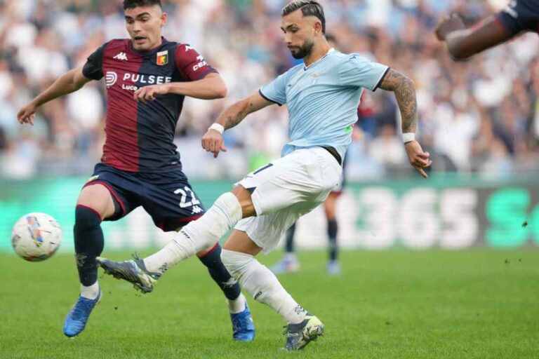 Durante Lazio-Genoa due calciatori si contendono un pallone in scivolata all'Olimpico, con maglie biancocelesti e rossoblù sotto gli spalti.