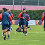 Giocatori del Genoa si allenano sul campo in maglia blu e rossa, con esercizi di corsa e riscaldamento in vista della sfida contro il Napoli al Ferraris.