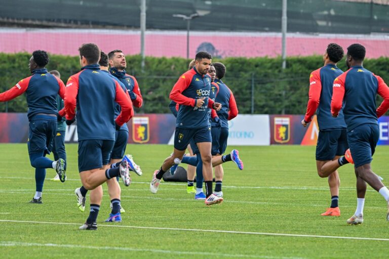 Giocatori del Genoa si allenano sul campo in maglia blu e rossa, con esercizi di corsa e riscaldamento in vista della sfida contro il Napoli al Ferraris.