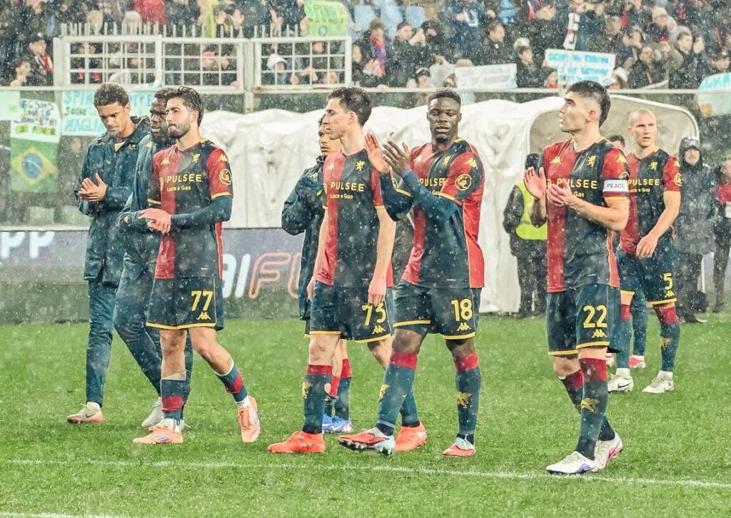 Nel post su Open Var, i giocatori del Genoa applaudono sotto la pioggia mentre il Napoli resta sullo sfondo dopo un episodio contestato.