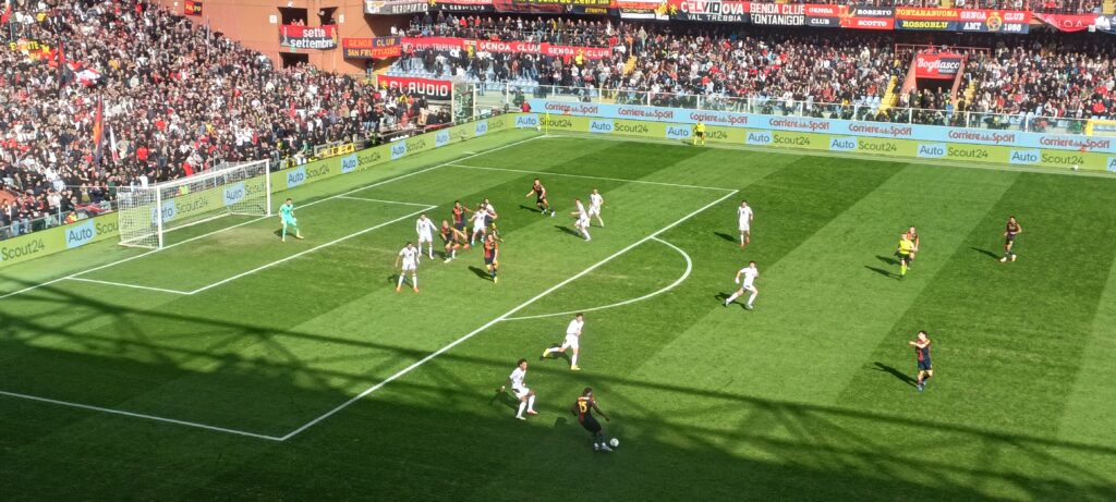Norton-Cuffy del Genoa avanza palla al piede nell'area avversaria durante la sfida salvezza contro il Torino, con lo stadio gremito e la difesa schierata.