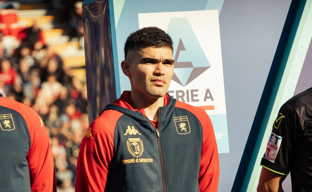 Un giocatore del Genoa in tuta rosso-blu con patch Comune di Sanremo aspetta l'ingresso in campo davanti al logo della Serie A.