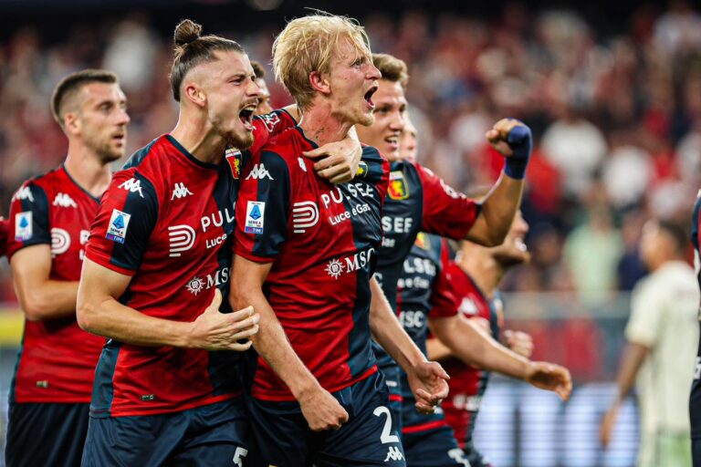 Morten Thorsby esulta con i compagni del Genoa in maglia rossoblù dopo una giocata decisiva, mentre lo stadio rumoreggia sullo sfondo.