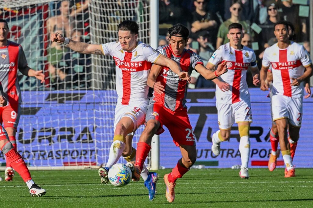 Nel match Cremonese-Genoa, Vitinha contende il pallone tra i difensori grigiorossi mentre il Genoa spinge nell'area avversaria.