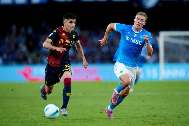 Nel Ferraris, un giocatore del Genoa in maglia rossoblù rincorre un avversario del Napoli in azzurro durante Genoa-Napoli, sfida intensa di campionato.