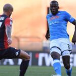 Un giocatore del Genoa in maglia rossoblù affronta un avversario del Napoli in azzurro durante la sfida Genoa-Napoli sul campo.