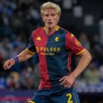 Morten Thorsby corre con la maglia rossoblù del Genoa, con numero 2 e sponsor PulseE, sullo sfondo di uno stadio sfocato.