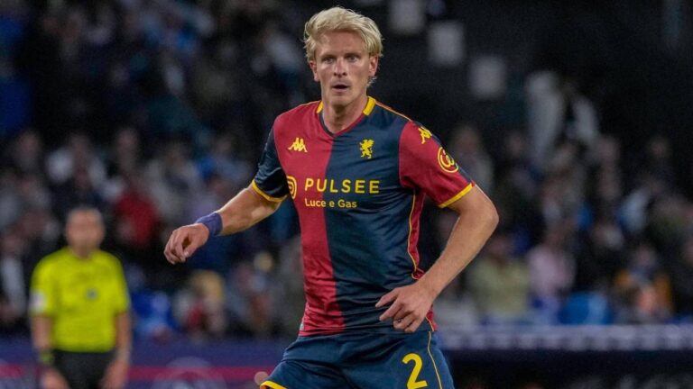 Morten Thorsby corre con la maglia rossoblù del Genoa, con numero 2 e sponsor PulseE, sullo sfondo di uno stadio sfocato.