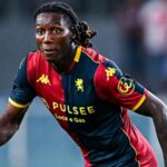 Calciatore in maglia rossoblù e blu con dettagli gialli corre in campo, Norton-Cuffy in primo piano, squadra Genoa in azione durante la partita.