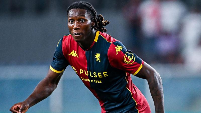 Calciatore in maglia rossoblù e blu con dettagli gialli corre in campo, Norton-Cuffy in primo piano, squadra Genoa in azione durante la partita.