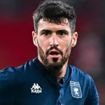 Aaron Martin, esterno sinistro del Genoa, in divisa blu scuro con stemma della squadra, viso concentrato durante una partita e controllo del pallone.