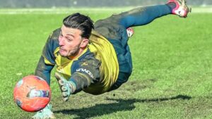 Bijlow portiere in volo, maglia gialla, guanti, pallone rosso in primo piano sul prato verde