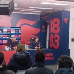 Sala stampa Genoa con pannelli rosso e blu e scritta 1893: De Rossi parla ai giornalisti mentre Patrizio Masini segue i lavori