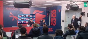 Sala stampa Genoa con pannelli rosso e blu e scritta 1893: De Rossi parla ai giornalisti mentre Patrizio Masini segue i lavori