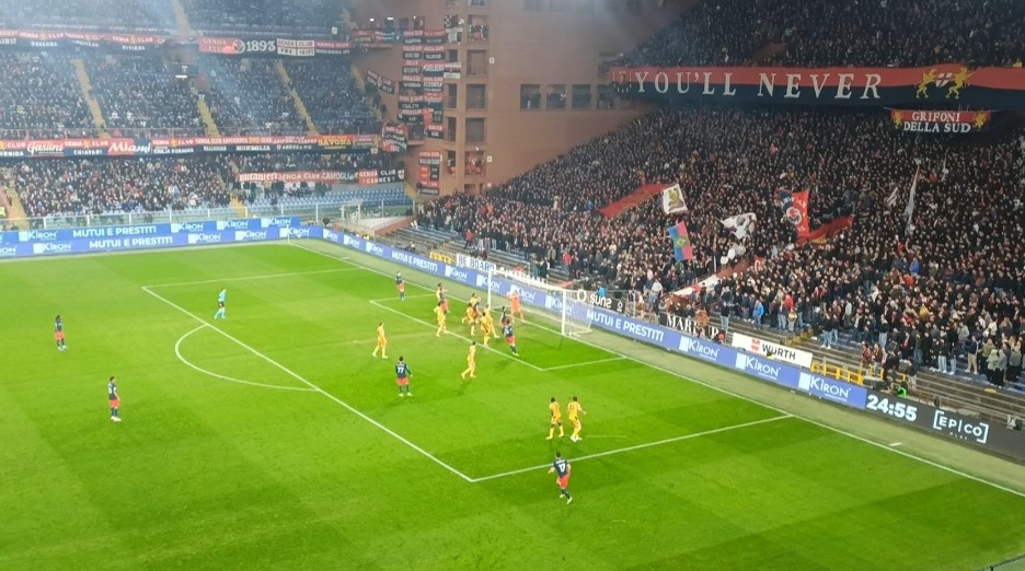 Malinovskyi tra i giocatori del Genoa in maglia rossoblu, tifosi in curva con striscioni, azione di calcio al stadio tra Genoa e Udinese durante una partita intensa