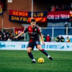 Malinosvkyi del Genoa in maglia rossoblù sul prato verde al Bentegodi, mentre controlla il pallone giallo. Verona-Genoa, finale salvezza.