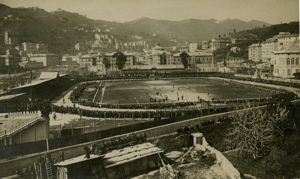 Veduta storica in stile sepia dello Stadio Ferraris e del Tempio di Marassi a Marassi, con il campo e le tribune gremite di pubblico.