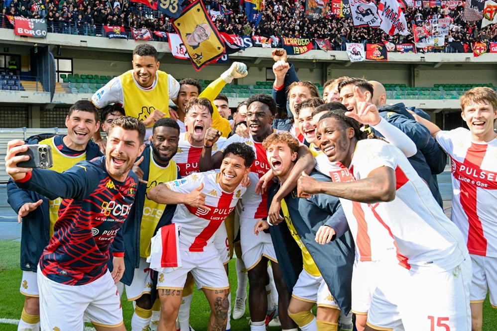 Genoa e Verona celebrano, giocatori in divise bianco-rosse e gialle, volti sorridenti, braccia alzate in festa sul prato, tifosi sugli spalti alimentano l'energia della scena