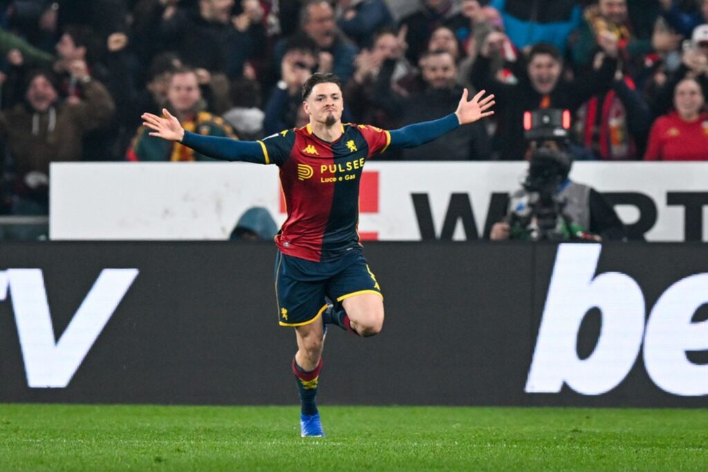 Vitinha in maglia rosso-blu del Genoa esulta con le braccia aperte sul campo durante la sfida Genoa–Roma, richiamata nelle pagelle.