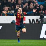 Vitinha in maglia rosso-blu del Genoa esulta con le braccia aperte sul campo durante la sfida Genoa–Roma, richiamata nelle pagelle.