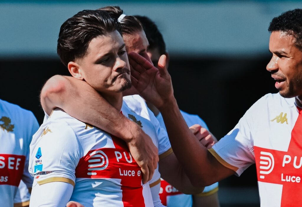 Vitinha tra i compagni in esultanza, accompagnato da Norton-Cuffy e Ostigard, nelrossover di gioco Genoa-Verona, maglie bianche con banda rossa e stemmi in evidenza