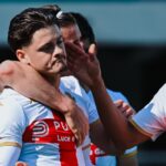 Vitinha tra i compagni in esultanza, accompagnato da Norton-Cuffy e Ostigard, nelrossover di gioco Genoa-Verona, maglie bianche con banda rossa e stemmi in evidenza