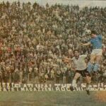 Beppe Savoldi in azione su campo verde, pubblico in tribuna e atmosfera anni ’60-’70, richiamo al leggendario bomber italiano del Napoli e Bologna.