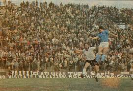 Beppe Savoldi in azione su campo verde, pubblico in tribuna e atmosfera anni ’60-’70, richiamo al leggendario bomber italiano del Napoli e Bologna.