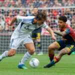 Contrasto in area tra Genoa e Como al Luigi Ferraris: calciatori in maglia bianco-blu contro divisa rosso-nera, palla in primo piano e rete sullo sfondo.