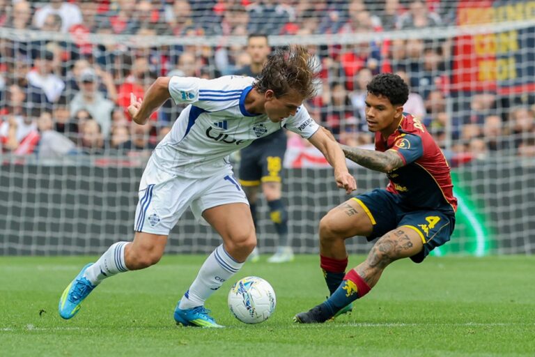 Contrasto in area tra Genoa e Como al Luigi Ferraris: calciatori in maglia bianco-blu contro divisa rosso-nera, palla in primo piano e rete sullo sfondo.