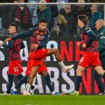 Genoa e Juventus in azione allo Juventus Stadium: giocatori in divise rosse e blu durante il riscaldamento, con l’allenatore Luciano Spalletti visibile sullo sfondo e Daniele De Rossi in primo piano.