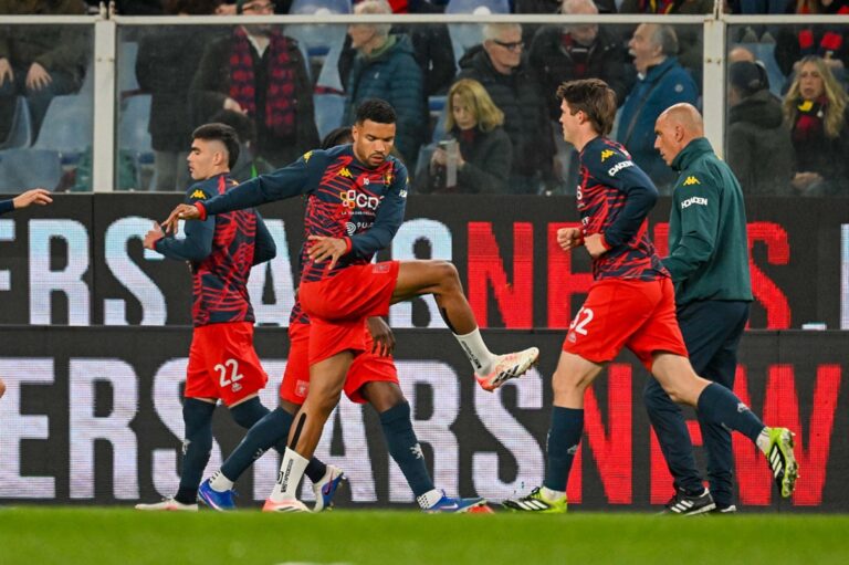 Genoa e Juventus in azione allo Juventus Stadium: giocatori in divise rosse e blu durante il riscaldamento, con l’allenatore Luciano Spalletti visibile sullo sfondo e Daniele De Rossi in primo piano.