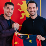 Stefano Sabelli in posa con la maglia rossoblù del Genoa, con sfondo rosso e blu: abbraccio e sorriso durante il rinnovo fino al 2028