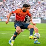 Ellertsson in maglia arancione del Genoa sfida un giocatore della Juventus su un prato verde, stando vicino al pallone e con crowd sugli spalti in sfondo