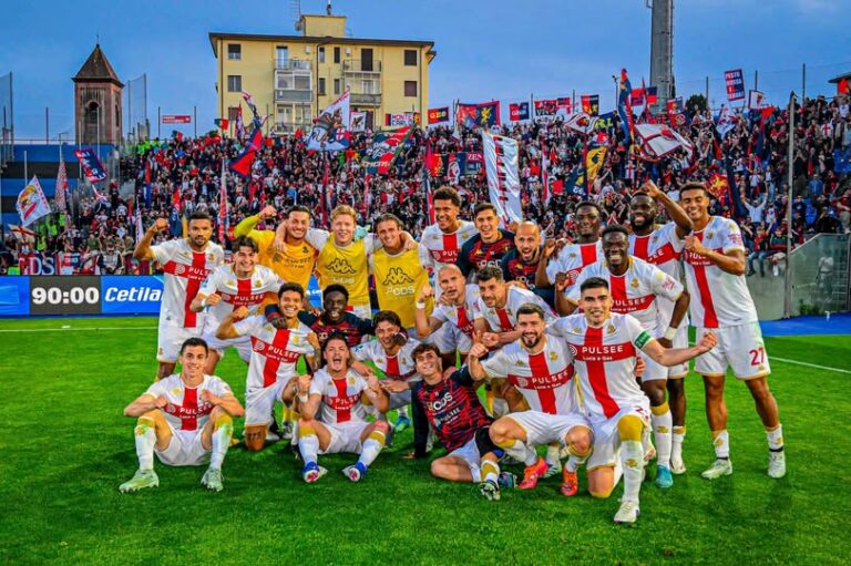 Giocatori del Genoa in festa con sciarpe e bandiere rossoblù davanti alla tifoseria: celebrazione nel derby Pisa–Genoa dopo la vittoria.