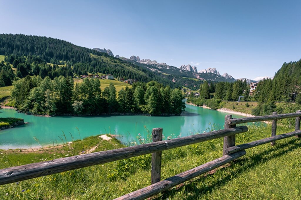Val di Fassa, lago turchese tra boschi verdi e montagne dolomitiche: panorama per il ritiro estivo del Genoa.