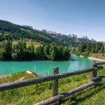 Val di Fassa, lago turchese tra boschi verdi e montagne dolomitiche: panorama per il ritiro estivo del Genoa.