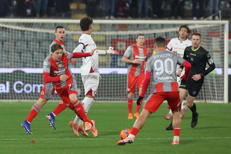 Cremonese contro Cagliari: giocatori in maglie rosse e pantaloncini grigi si contendono il pallone davanti alla porta, con un overall dinamico e intenso della partita tra Cremonese e Cagliari, presenza di Pinamonti in campo