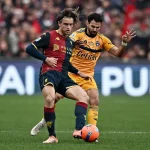 Azione in campo tra Genoa e Pisa: giocatori in maglia rossoblù e giallo-arancio contrastano sul pallone, con Colombo in evidenza.