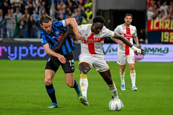 Contrasto in Atalanta-Genoa con Ekhator in maglia blu-nero, avversario in bianco-rosso, palla in gioco: intensità e grinta da partita combattuta.